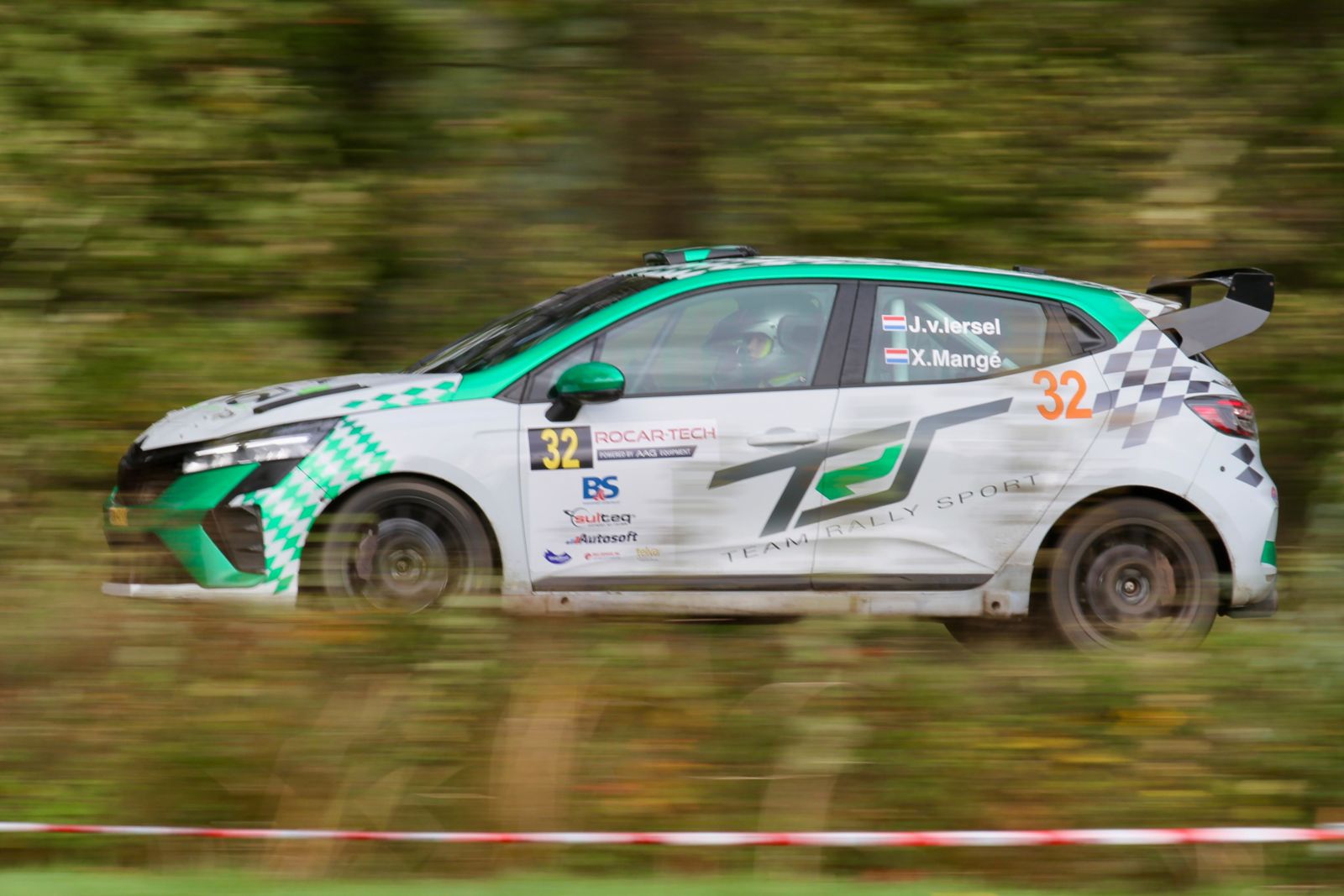 Panning shot of a green and white Renault Clio Rally3 racing past blurred autumn trees