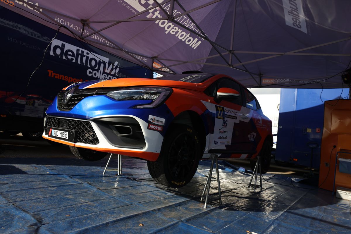 Orange and blue Renault Clio Rally4 on stands in a service tent
